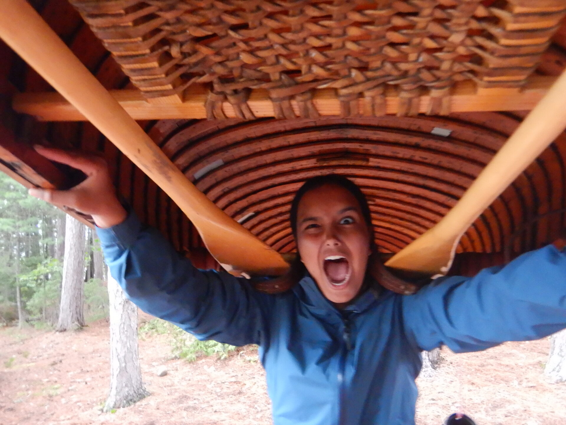 Person carrying canoe on shoulders in forest.