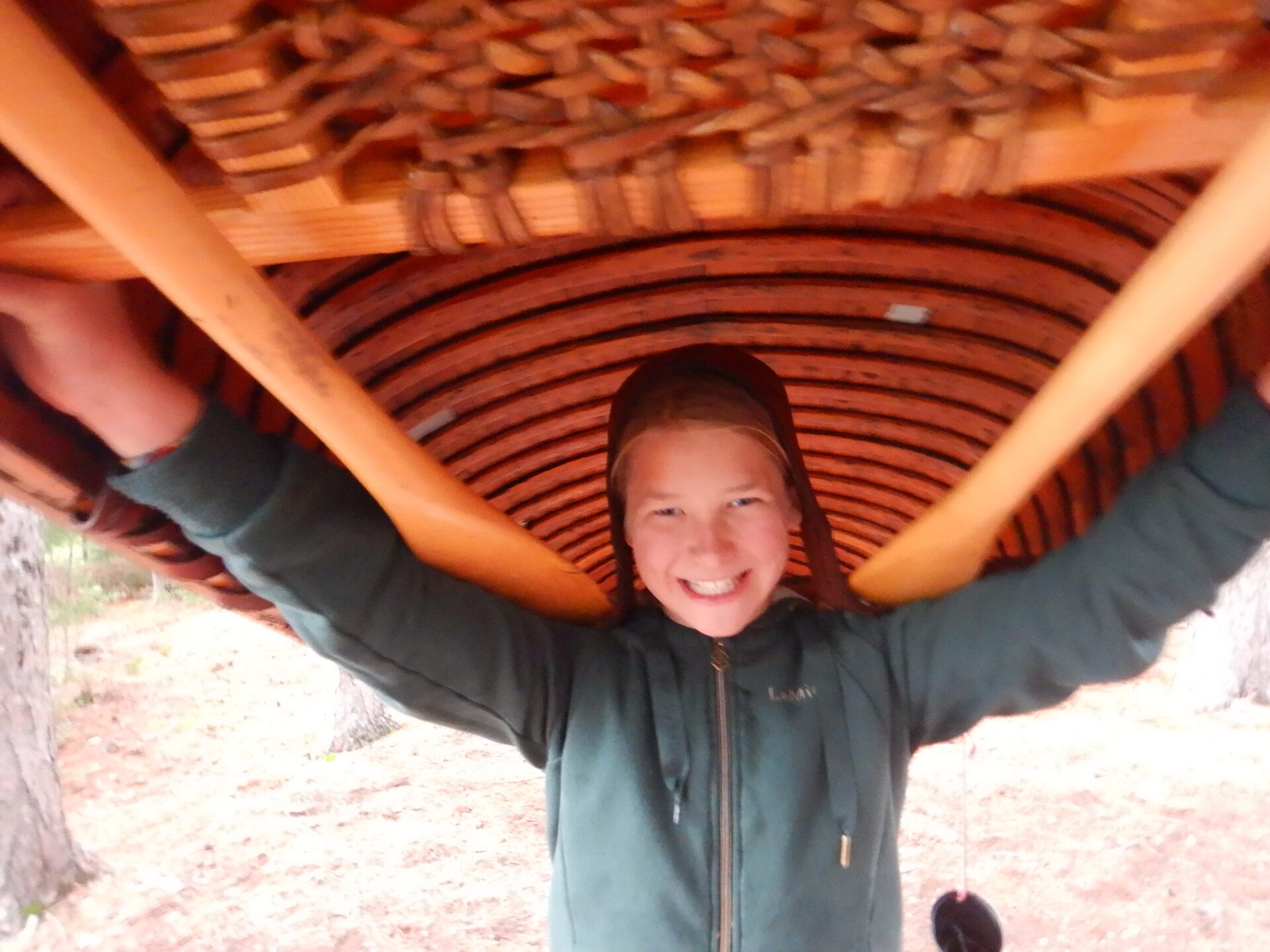 Child carrying wooden canoe on shoulders.