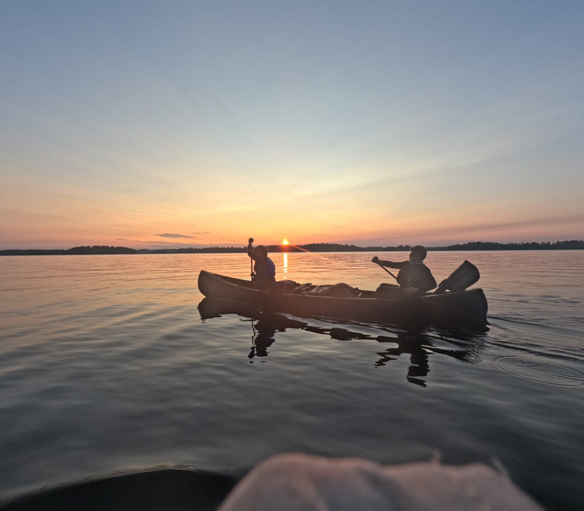 Two people canoeing at sunset on a lake.