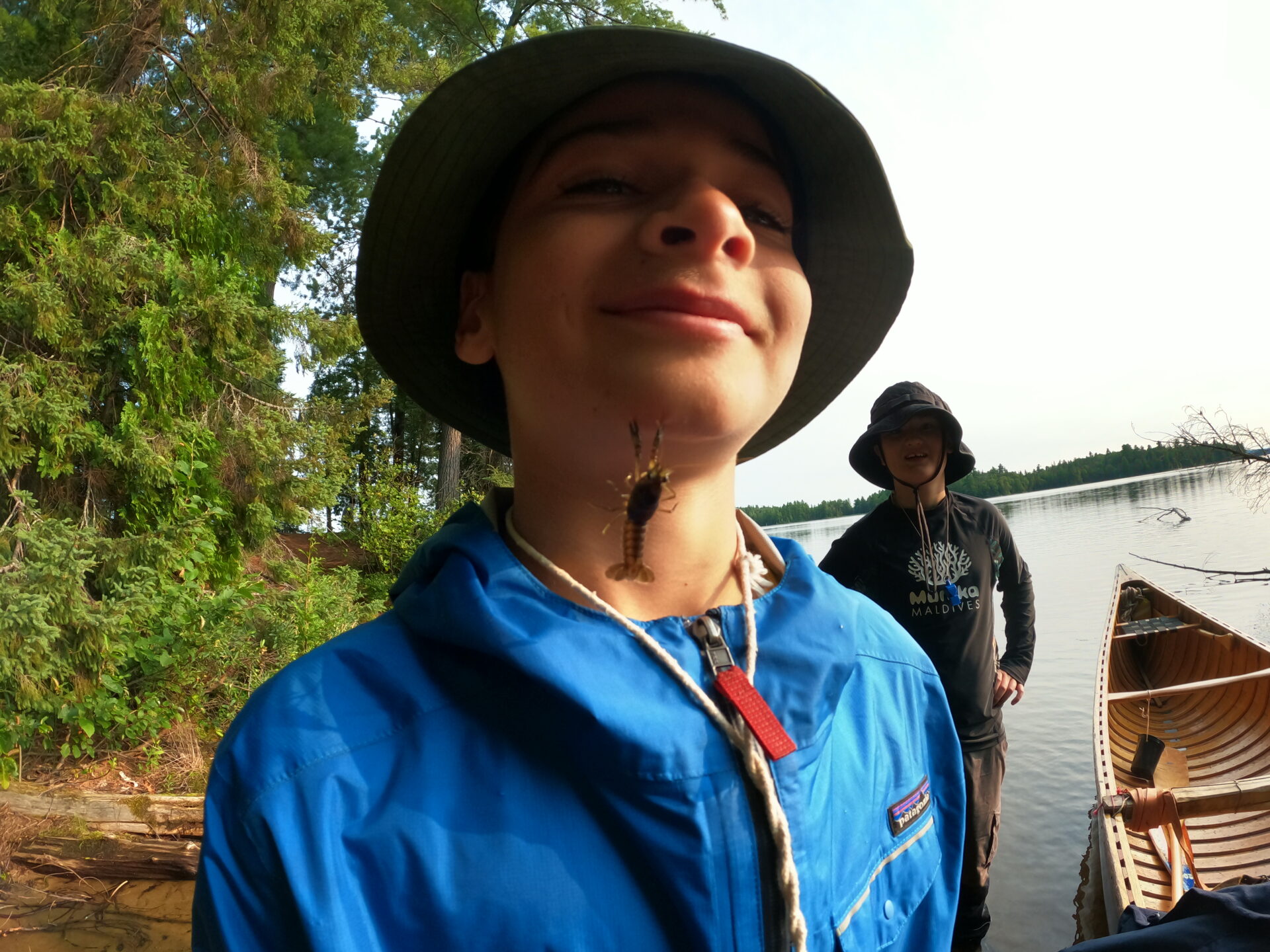 Smiling kid with frog on neck near canoe.