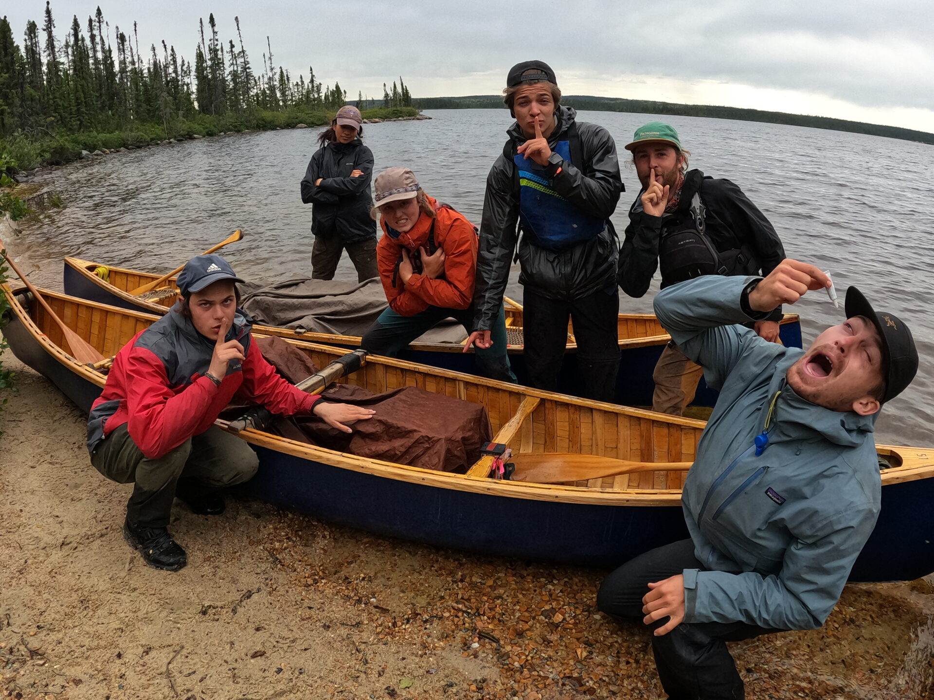 Group posing by canoes on a lakeshore