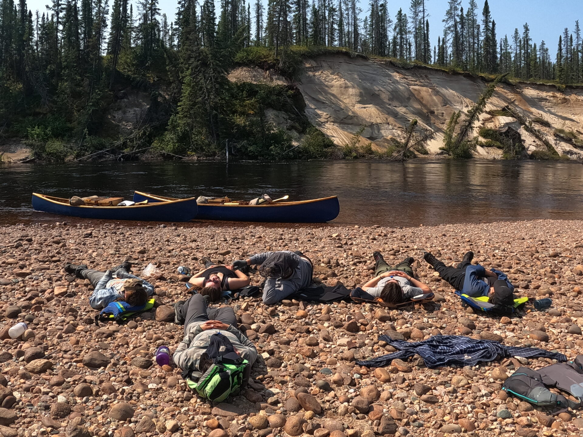 Group resting by river with canoes