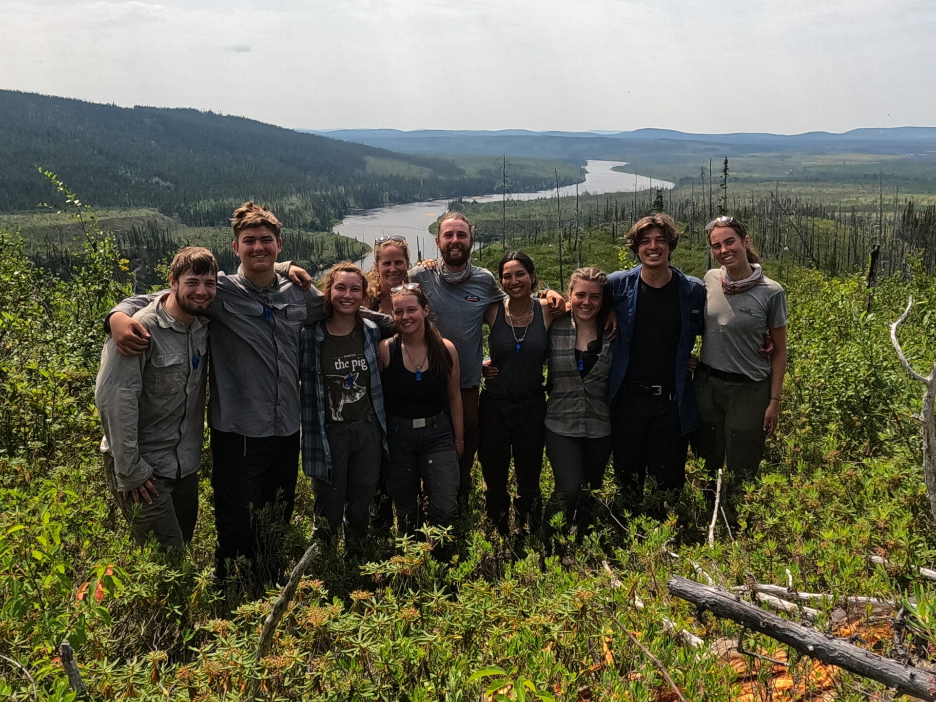 Group hiking in lush green forest with river view.