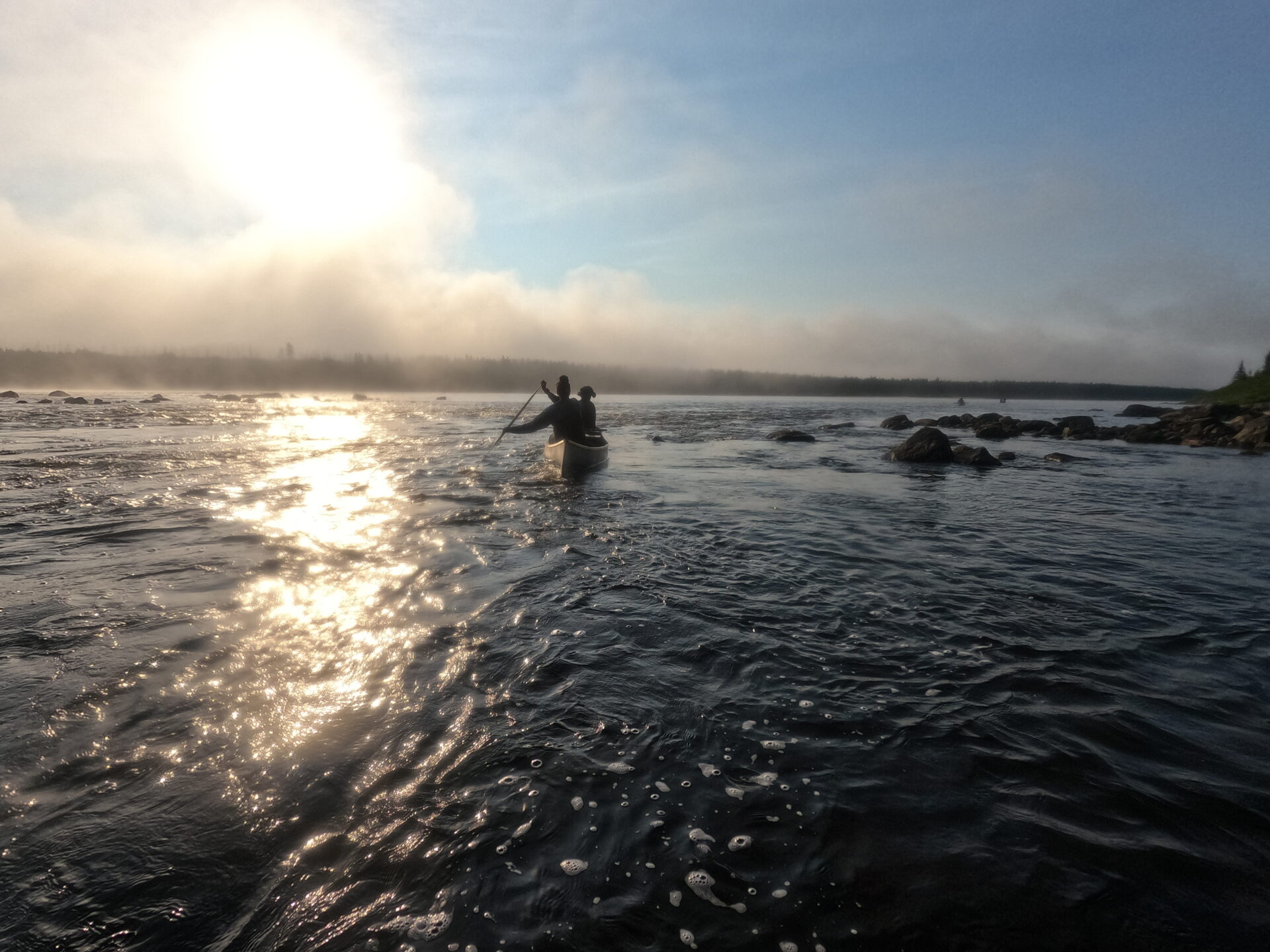 Two people canoeing at sunrise on a river.