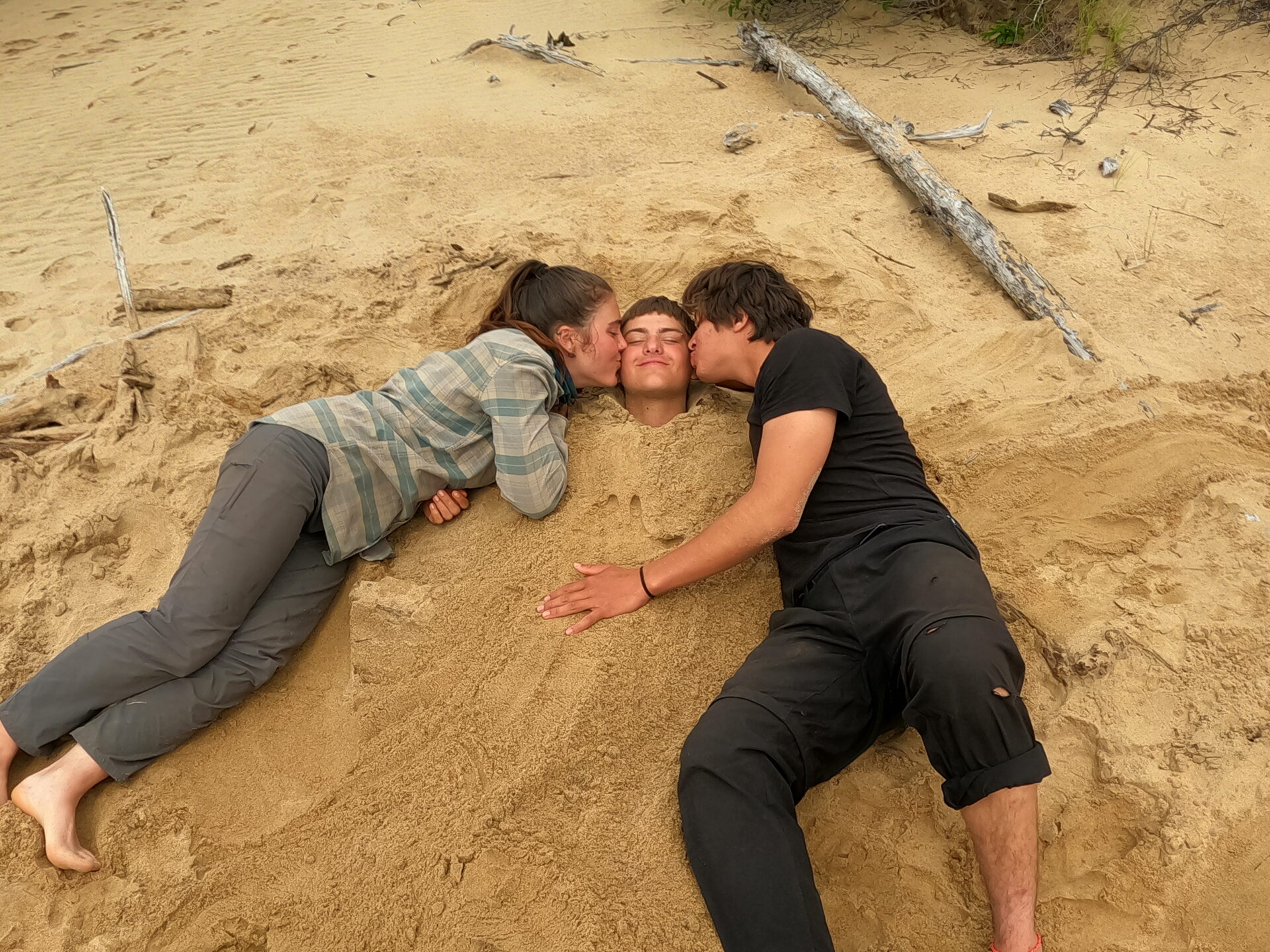 Friends bury in sand, kiss buried friend.