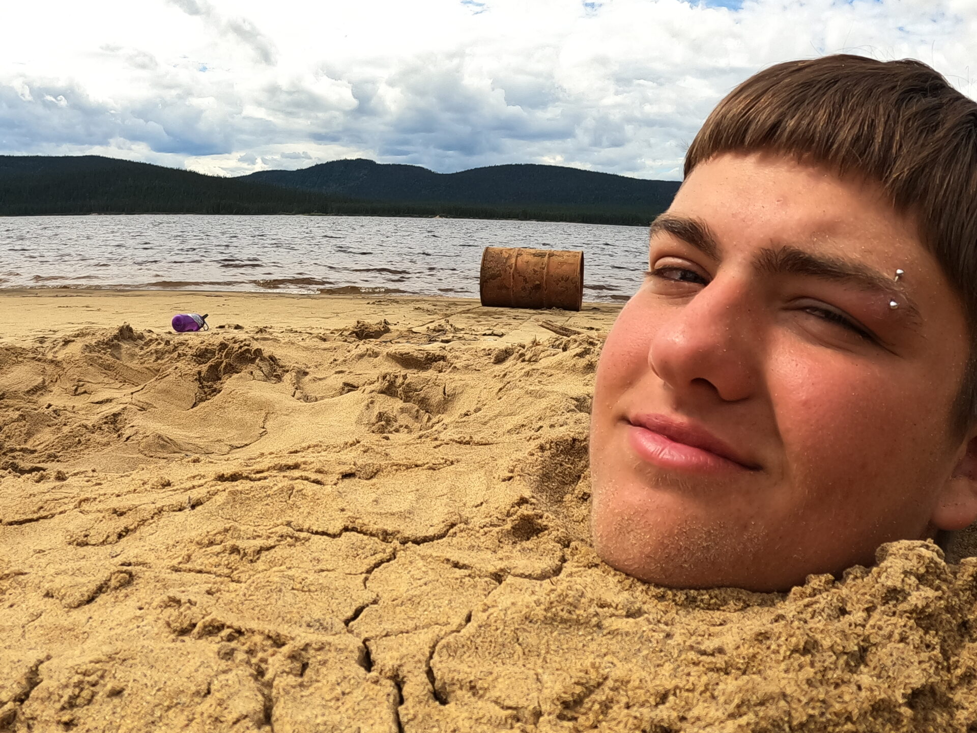 Head buried in sand at lakeside beach.