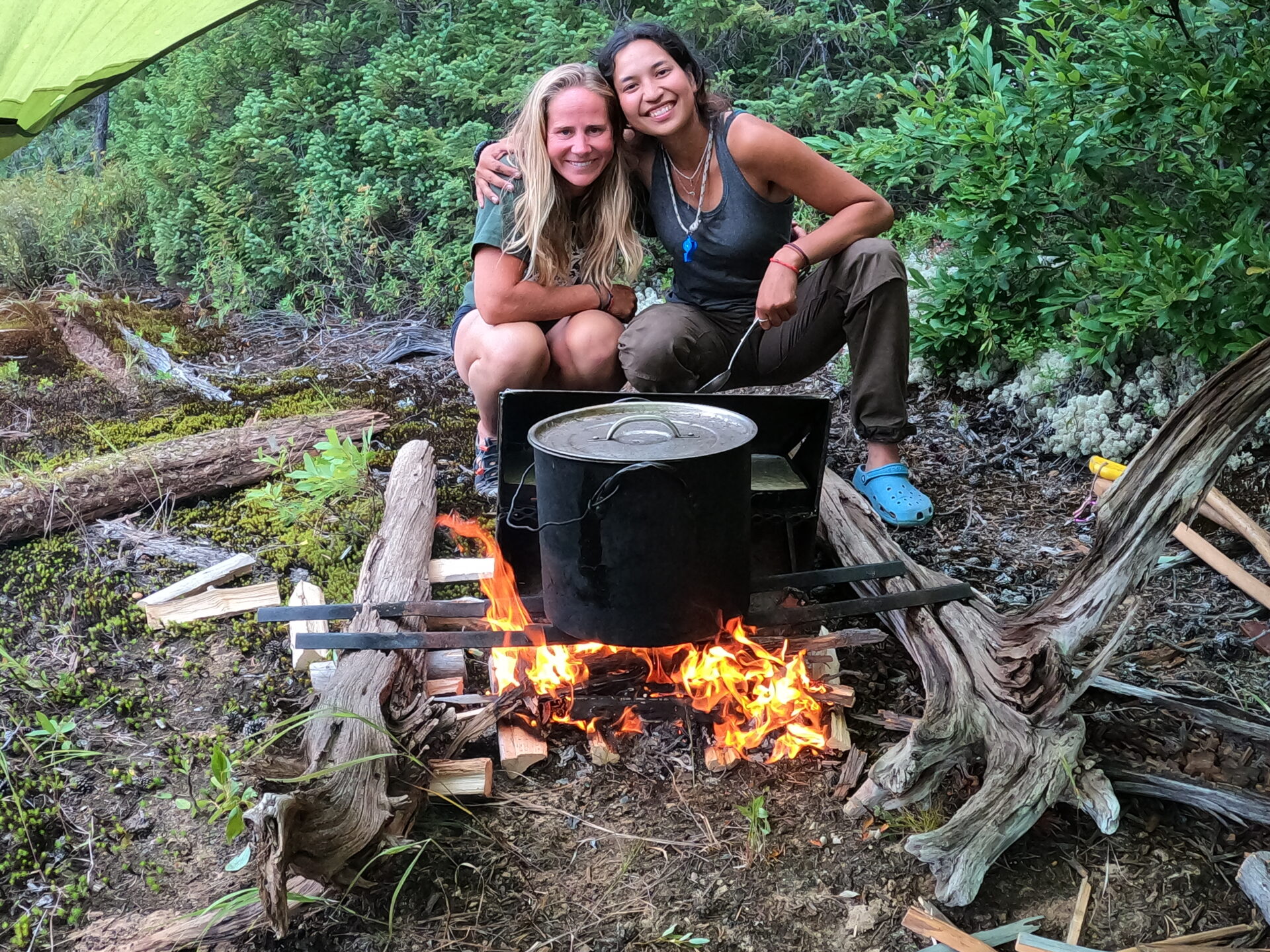 Two women camping near fire and cooking pot