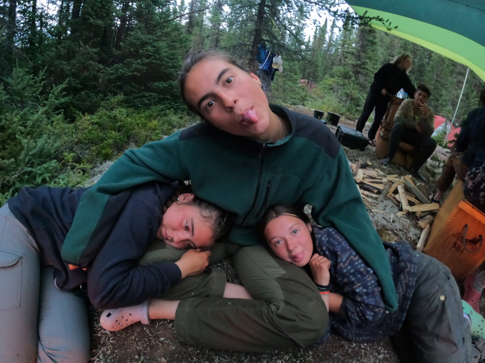 Three friends camping in the woods, playful and relaxed.