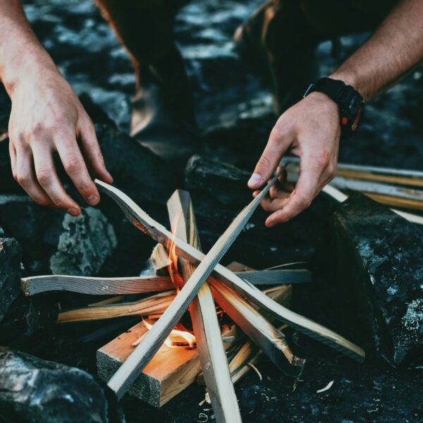 Hands starting a campfire with kindling.