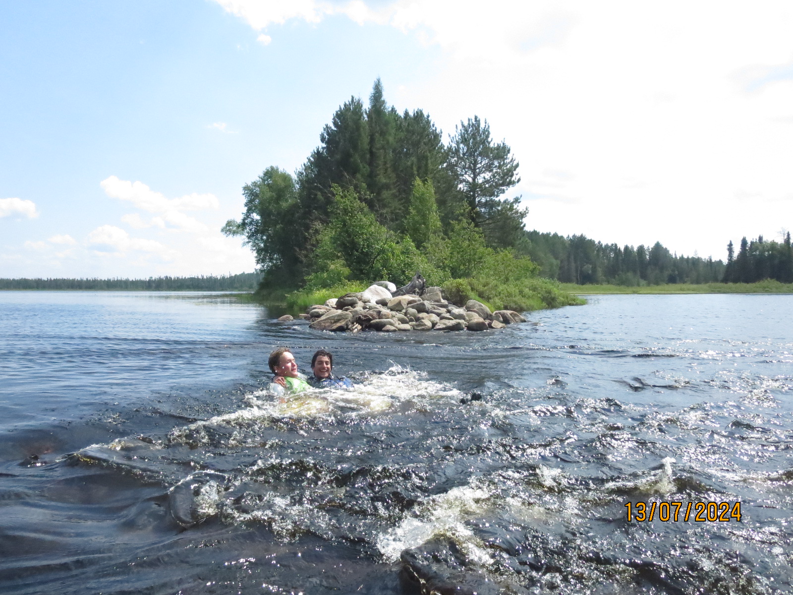 Two people swimming in a lake with forest.