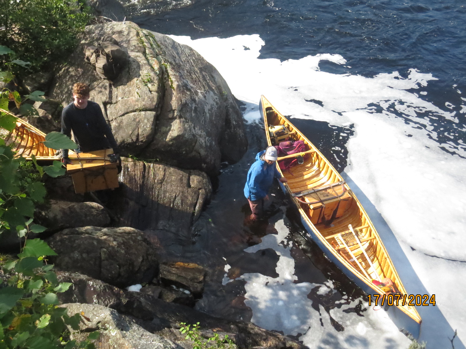 People portaging a canoe beside rocky shore.