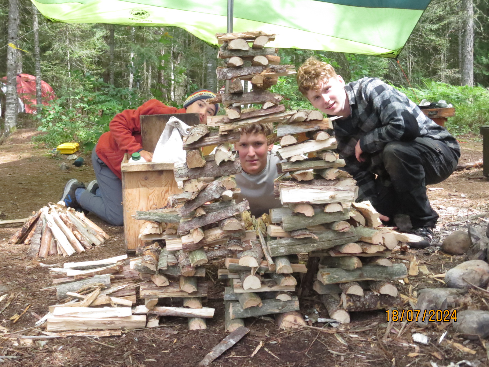 Three boys building a log structure in forest