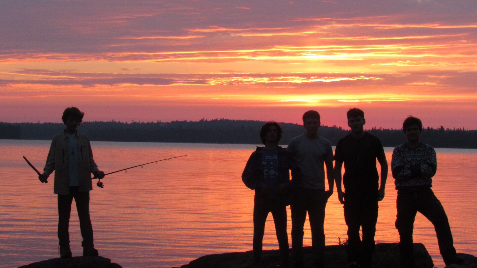 People standing by lake at sunset.