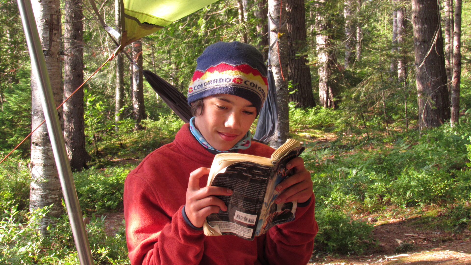 Person wearing a hat reading a book outdoors.