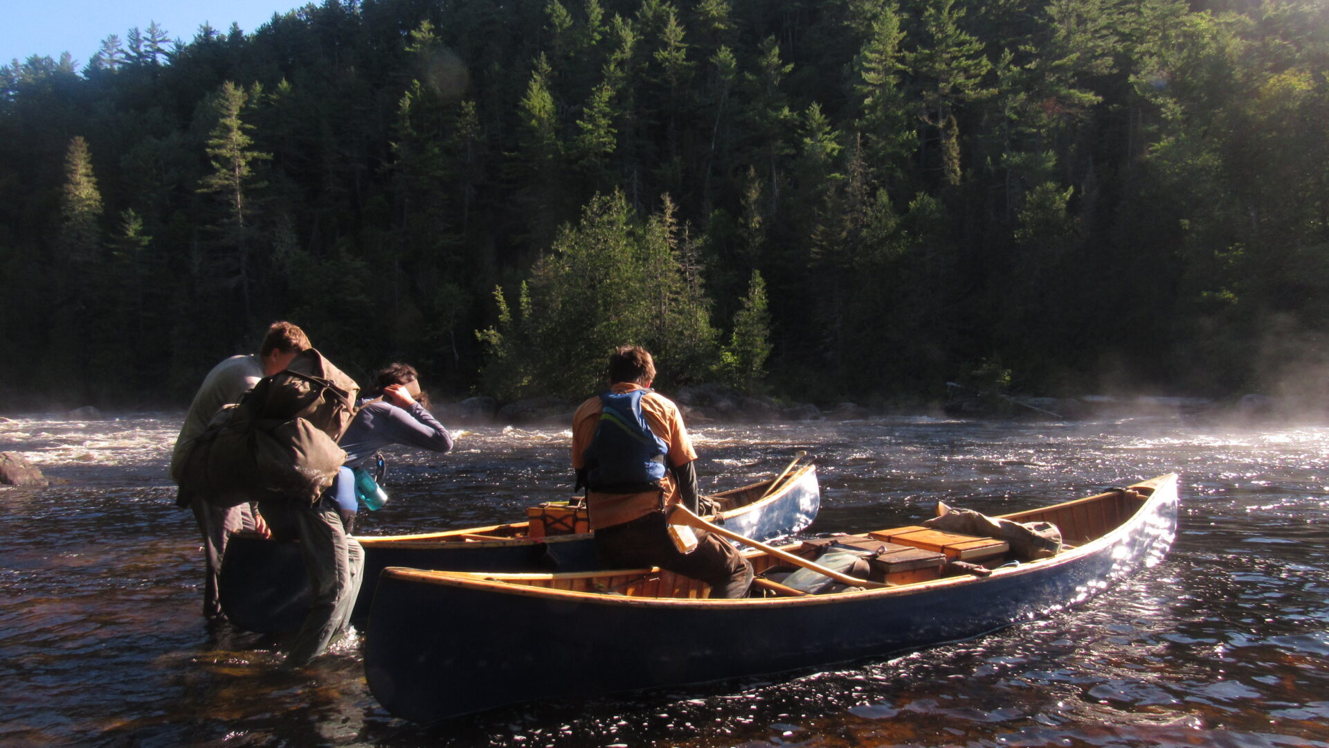 Three people launching canoes on a forest river.