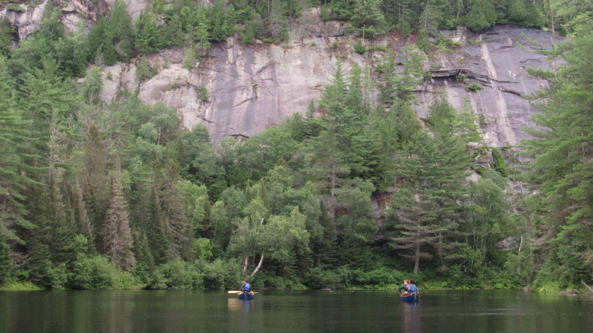 Kayakers on lake near forest and cliff.