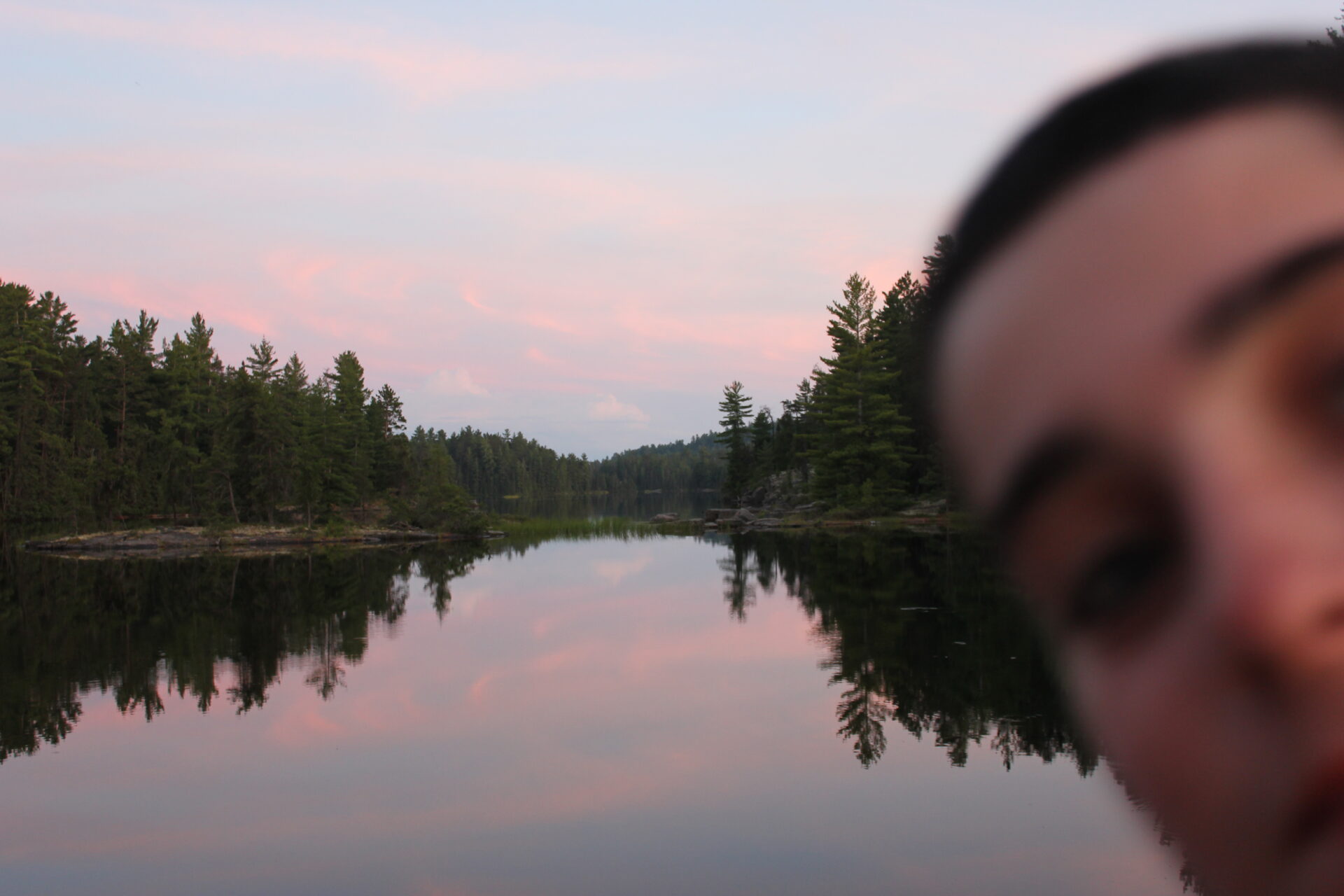 Reflection of trees on calm lake at sunset.