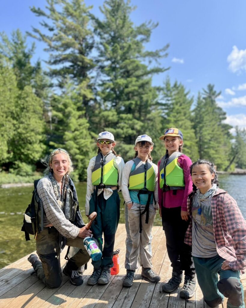 Group of kids in life vests by lake.