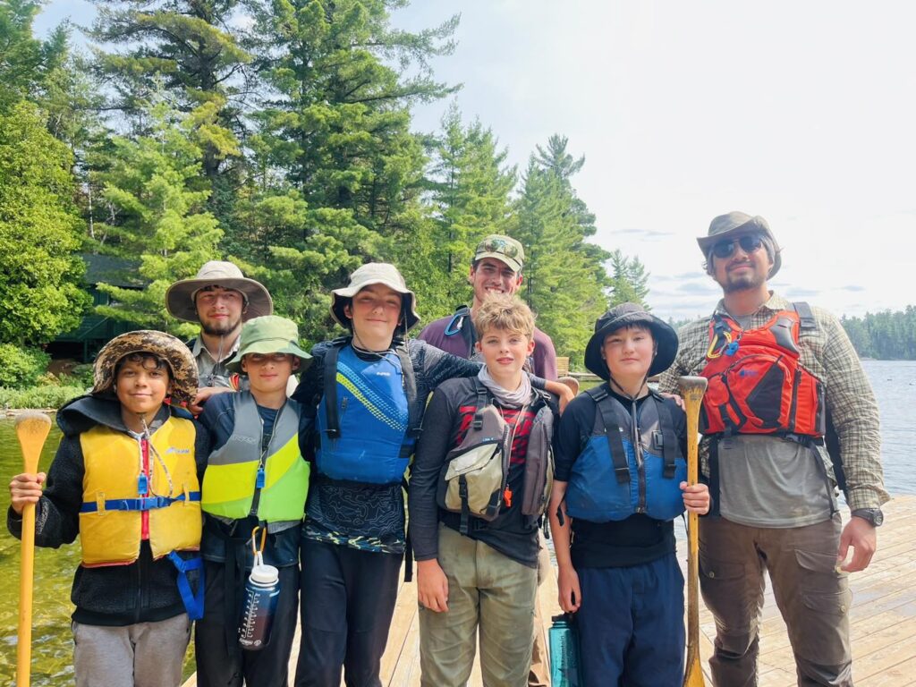 Group posing in life vests at lakeside.