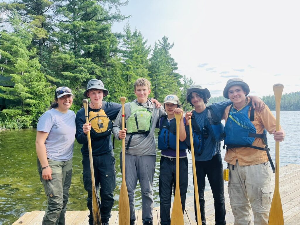 Group smiling with paddles by a lake.