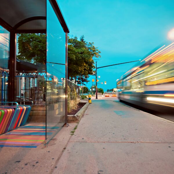 Bus passing colorful bus stop at twilight.