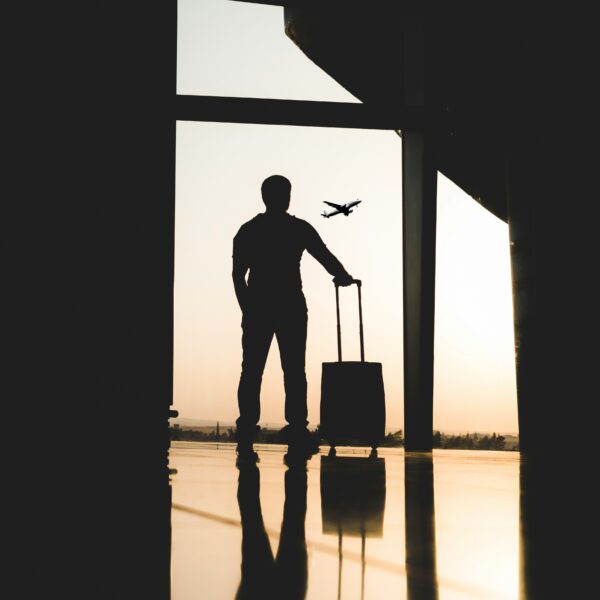 Traveler at airport with luggage, plane in sky.