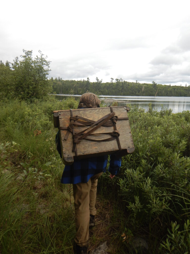 Person hiking with wannigan near lake and trees.