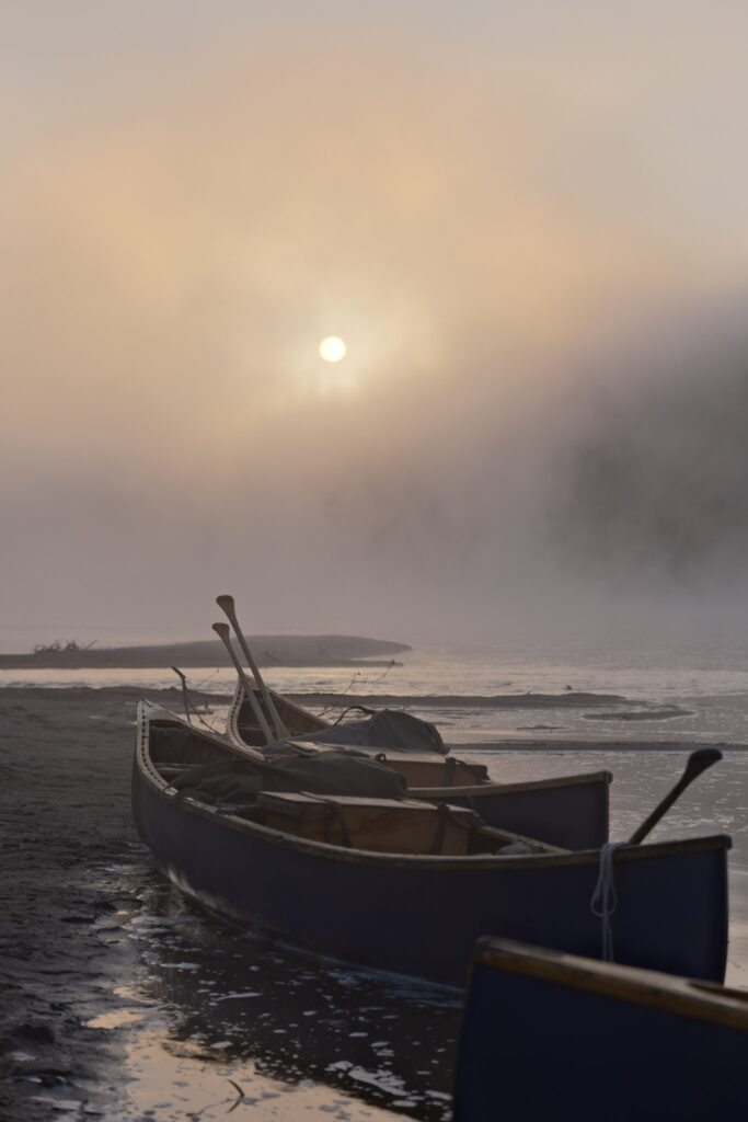 Canoes on misty riverbank at sunrise