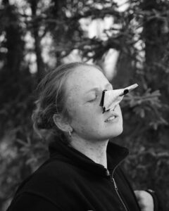 Person balancing paper bird on nose outdoors.