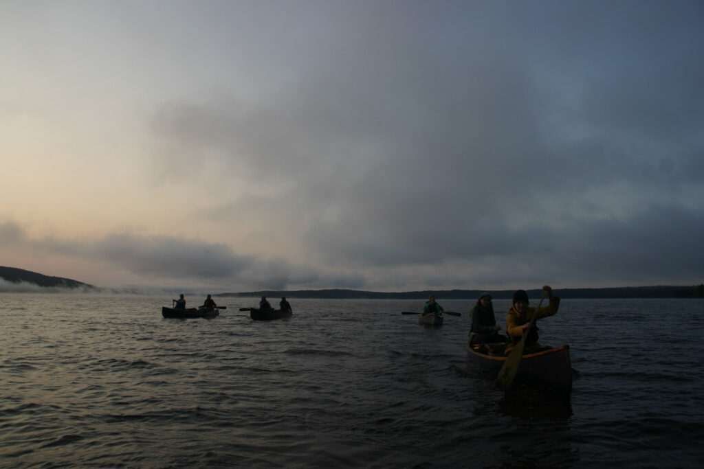 People canoeing on a misty lake at dawn.