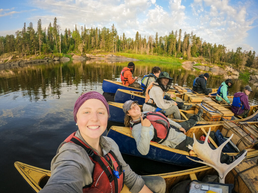 Group canoeing on scenic lake with forest background.