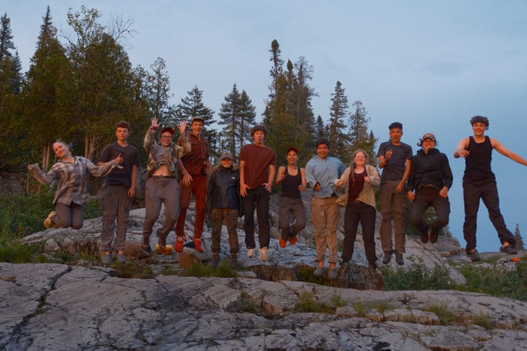 Group of friends jumping outdoors on rocky terrain.