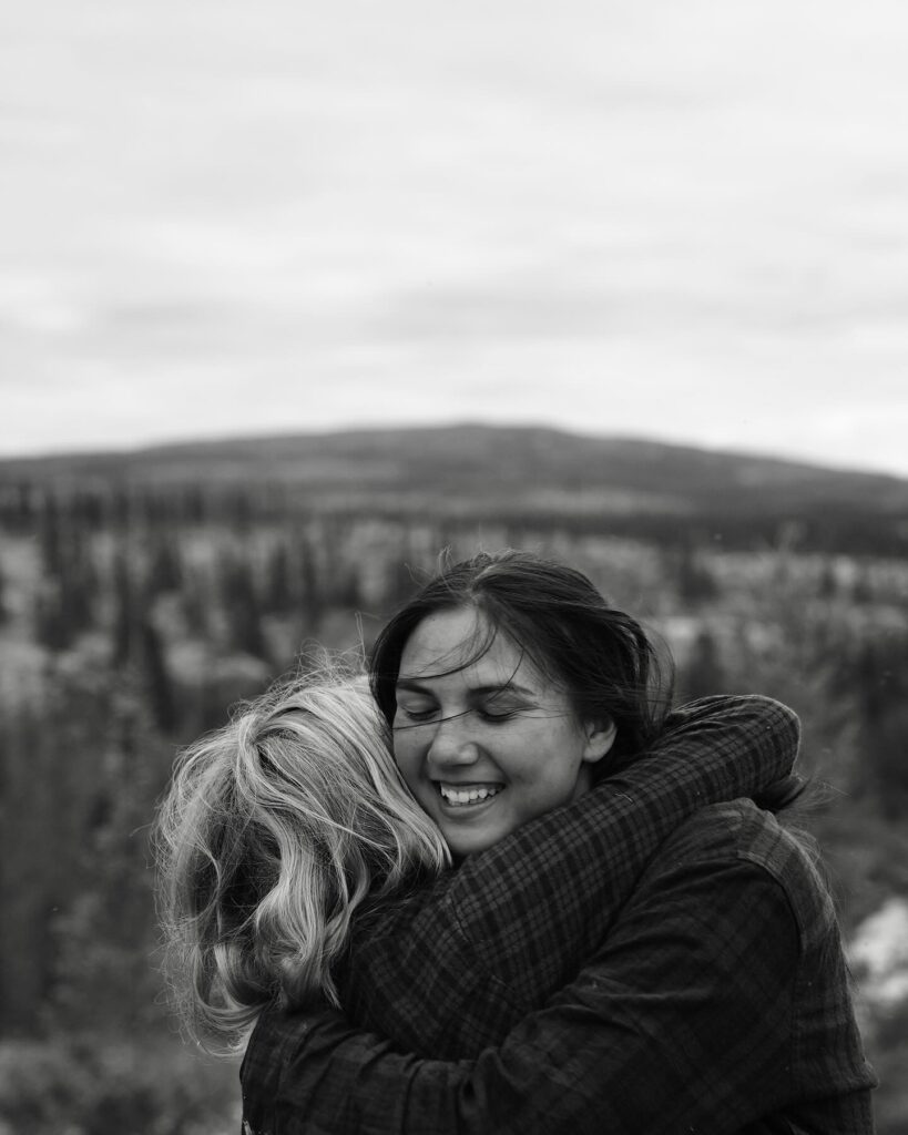 Two women hugging outdoors, smiling warmly.