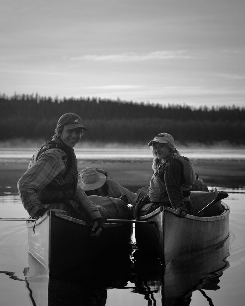 People smiling while canoeing on a tranquil lake.