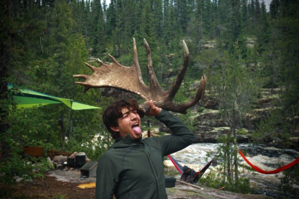 Person posing with moose antler in forest.