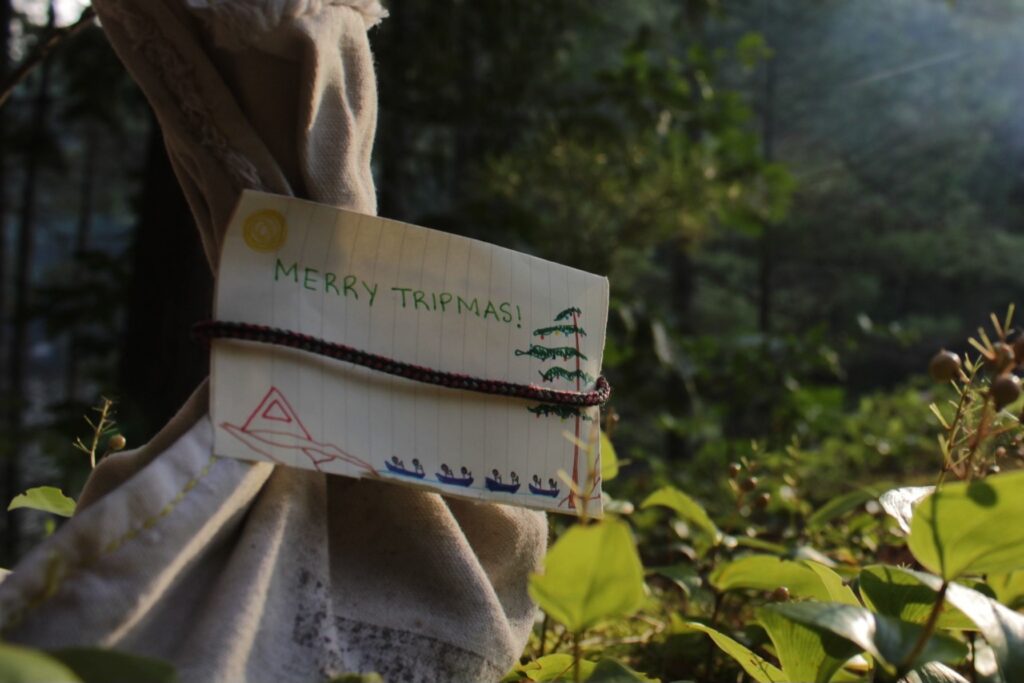 Paper note with 'Merry Tripmas' in forest.