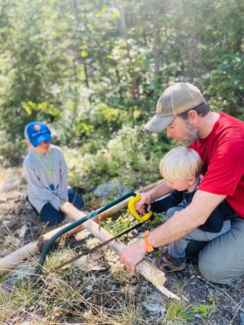 Family sawing logs outdoors in a forest.