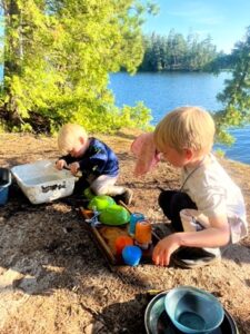 Children doing dishes by a lakeside.