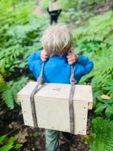 Child carrying wooden box in forest trail