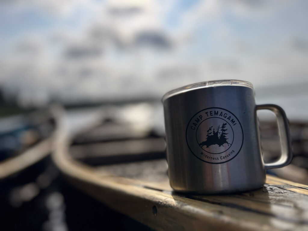 Camp mug on canoe, blurred lake background.